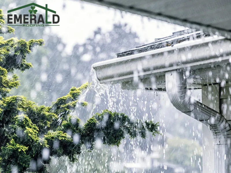 Heavy rain flowing off roof gutter during a storm, showing potential storm damage to residential roofing